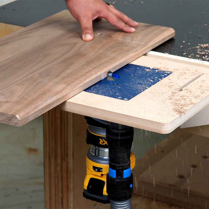 Router table in use with a piece of wood on top, showing woodworking process.