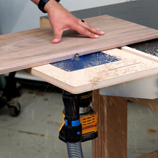 Person using a router table with a piece of wood on a workshop surface.